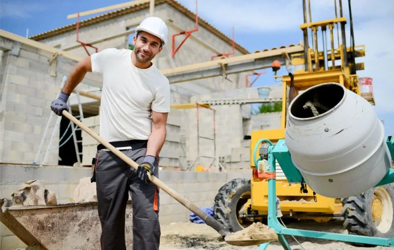 A builder on a job site with a shovel and cement mixer